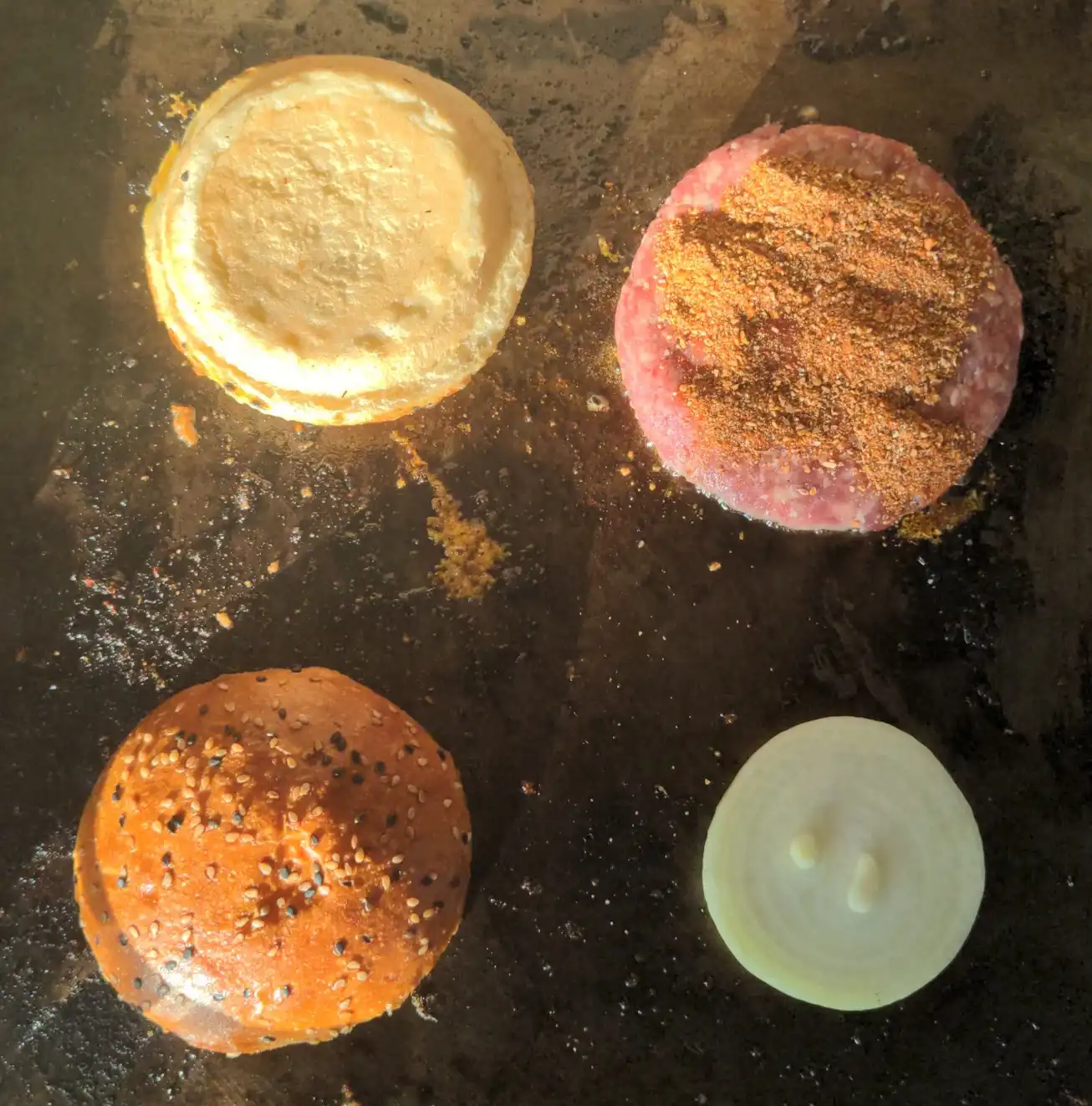 Arranged buns, seasoned patty, and onion slice on the grill.