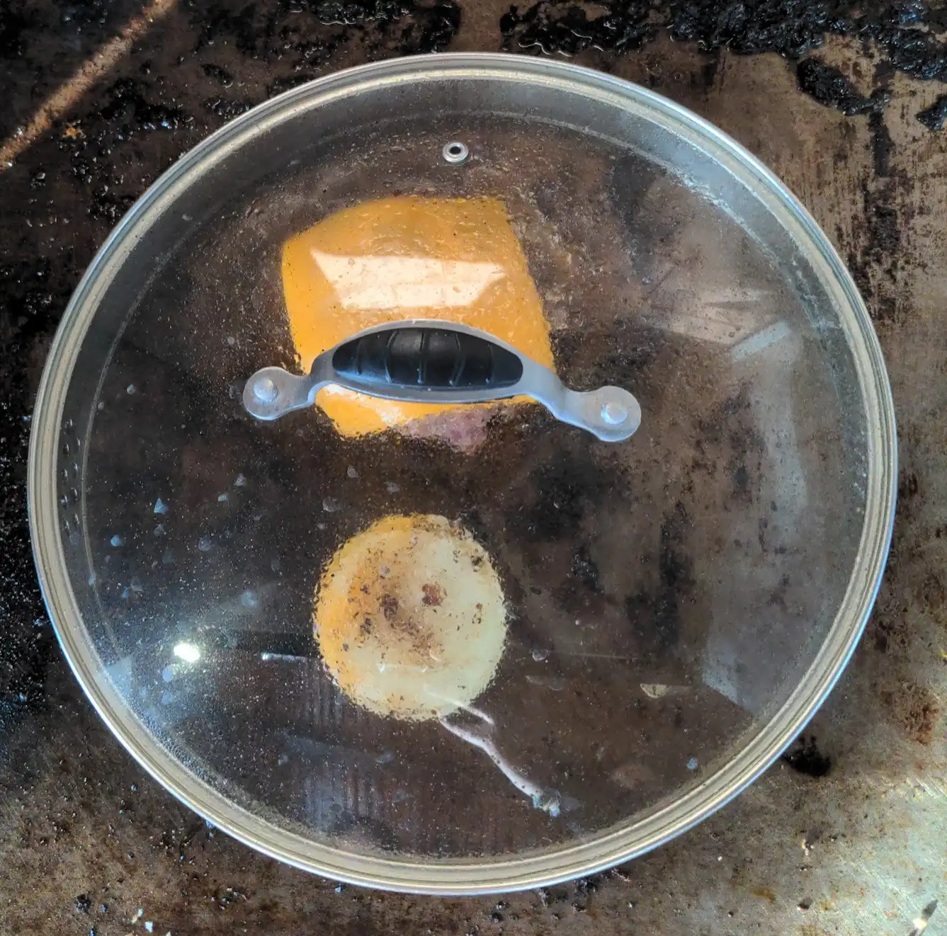 Cheese on top of patty, covered by a lid.